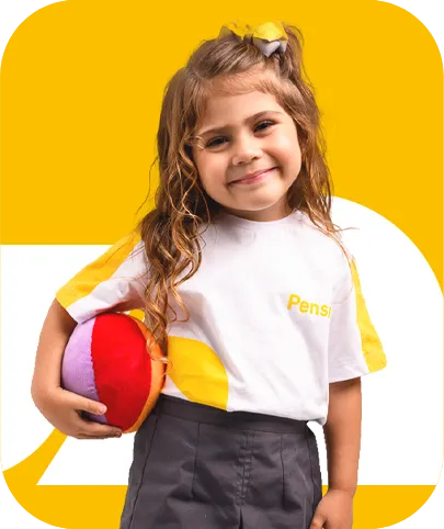 Menina sorridente, aluna da Educação Infantil, usando uniforme escolar e segurando uma bola colorida